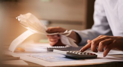 Close-up of economist using calculator while going through bills and taxes in the office.